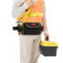 A waist tool bag in black with red accents, worn by a person holding a yellow tool box and wearing a high-visibility vest.