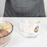 A clear glass baking measuring jug with markings for cups and millilitres, alongside bowls of ingredients.