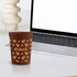 A brown plastic stadium cup featuring various designs and patterns, placed next to a laptop on a white table.