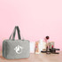 A grey hanging toiletry bag with two handles, placed on a table alongside various beauty products and tools.