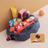 A navy and red foldable shopping shoulder bag filled with snacks, beverages, an apple, and an orange.
