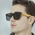 Bamboo sunglasses featuring black frames and wooden bamboo arms, modelled by a young man.