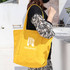 A yellow canvas zippered tote shoulder bag with a logo, carried by a person in a black outfit.