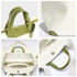 A cream canvas bag with a green leather handle, featuring detailed stitching and a snap closure.