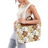 A canvas bag with a floral pattern in cream, brown, and green, featuring a leather handle. 