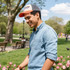 A young man wearing a distressed cotton baseball cap with a grey and orange design, standing in a park.