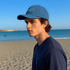A vintage washed baseball cap in light blue worn by a young man at the beach, with the ocean in the background.