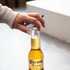 A drink bottle with a gold liquid and a black and white bottle opener being placed on top.