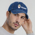 A denim baseball cap featuring a logo and white stitching, worn by a model with short hair and a neutral sweater.