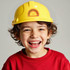 A yellow PVC construction hat worn by a smiling child, with a logo on the front.