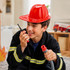 A bright red PVC fire chief hat is worn by a boy holding a walkie-talkie, dressed in a firefighter costume.