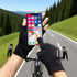Fingerless black sun protection gloves held up to a smartphone, with a scenic road and trees in the background.