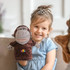 A plush monkey hand puppet in brown, held by a smiling child with a tiara, on a couch.