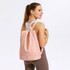 A pink backpack with a handle and adjustable straps, featuring a logo on the front.