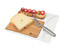 A cheese board with a wooden base, a cheese wedge, a stainless steel knife, and assorted snacks in a white tray.