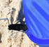 A blue beach shelter partially buried in sand, secured with a black strap and peg for stability.