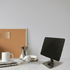A sleek, foldable metal tablet stand in black, positioned on a desk with a mug, headphones, and stationery.