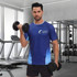 A man in a blue and light blue raglan tee shirt holds dumbbells in a gym setting, featuring a logo.