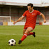 A male model wears red sports shorts with white trim, kicking a black and white soccer ball on a grassy field.
