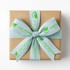 A gift box wrapped in brown paper, featuring a light blue satin ribbon with a logo and text printed on it.