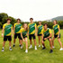 A group of six individuals wearing yellow and green polyester sports tee shirts poses outdoors on grass.