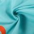 A close-up of light blue fabric, featuring a subtle swirl pattern and an orange design element.