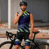 A man's cycling vest in purple and green with geometric patterns, worn with a helmet next to a bicycle.