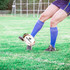 A promotional rugby ball on the ground, featuring a logo, with a player in blue socks preparing to kick it.