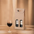 A portable wine box in brown with two compartments for bottles, alongside a glass of red wine.