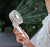 A white foldable USB hand fan is held in a person's hand, with air blowing from its grille. It features a logo.
