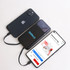 A black power bank with a logo, charging two smartphones on a light surface. The power bank has a sleek design.