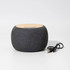 A round, grey wireless speaker with a wooden top and a USB cable beside it.
