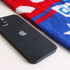 A black smartphone lies beside a red and blue jacquard sweater, featuring a playful pattern. The sweater has a logo.