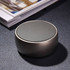 A round, grey wireless speaker with a textured grille, resting on a dark surface beside a stack of magazines.