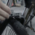 A multi-tool in metallic grey being used on a bike's fork and wheel, featuring a black tyre with a textured pattern.