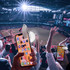 A smartphone with a white torch attachment, held by a person in a crowd at a sports event, surrounded by cheering fans.