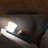 A compact white torch attached to a smartphone, illuminating a book in a dimly lit setting.