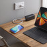 A black laptop power bank is charging an iPhone and connected to a laptop on a wooden table.
