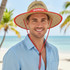A natural straw hat with a wide brim and red detailing, worn by a man on a beach.