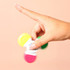 A hand spins a multi-coloured highlighter with pink, yellow, green, and orange caps against a peach background. A hand spins a multi-coloured highlighter with pink, yellow, green, and orange caps against a peach background.