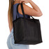 A black cooler bag with sturdy handles, carried by a person in a casual outfit. The bag features a logo.