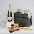 A grey cooler bag with a blanket, two glasses, a bottle of Chandon, a cheese board, and gourmet products inside.