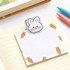 A notepad features a cute bunny-shaped clip and is decorated with small orange carrots. It has a pastel colour scheme.