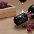 A drink bottle in black with a push button wine stopper, surrounded by red grapes and a wooden crate.