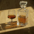 A crystal decanter and a snifter glass filled with amber liquid sit on a wooden surface, casting soft shadows. A crystal decanter and a snifter glass filled with amber liquid sit on a wooden surface, casting soft shadows.