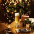 A goblet glass filled with golden beer sits on a table decorated with wrapped presents and a festive, blurred Christmas tree.