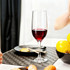 A classic wine glass filled with red wine, placed on a table alongside a plate and a bowl of lemons.