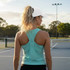 A woman with a ponytail wears a mint green athletic tank top and a white cap, standing on a tennis court.