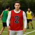 A red reversible training bib featuring the number 2, with a logo, worn by a man on a sports field.
