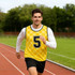 A yellow and black checkered training bib worn by a man running on a track, featuring a logo.